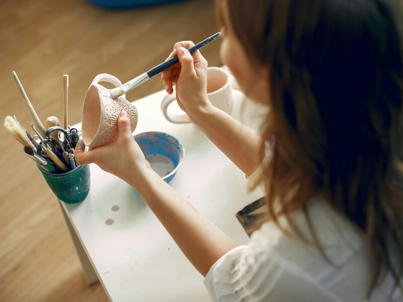 Woman seen from behind painting a ceramic mug
